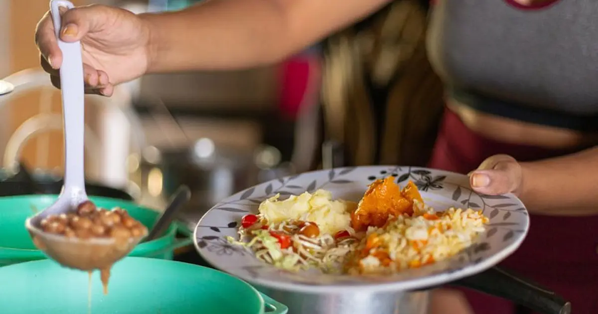 Mulher servindo comida no prato durante ação de segurança alimentar.