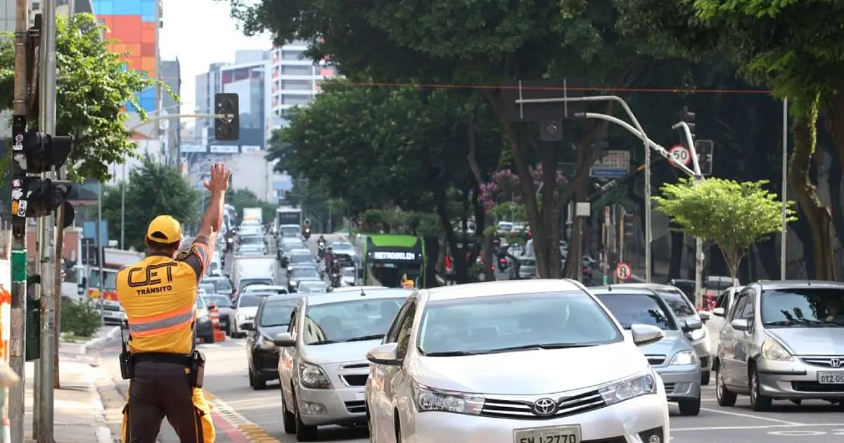 Condutores em via urbana com trânsito intenso e fiscalização de multas de trânsito no Brasil.