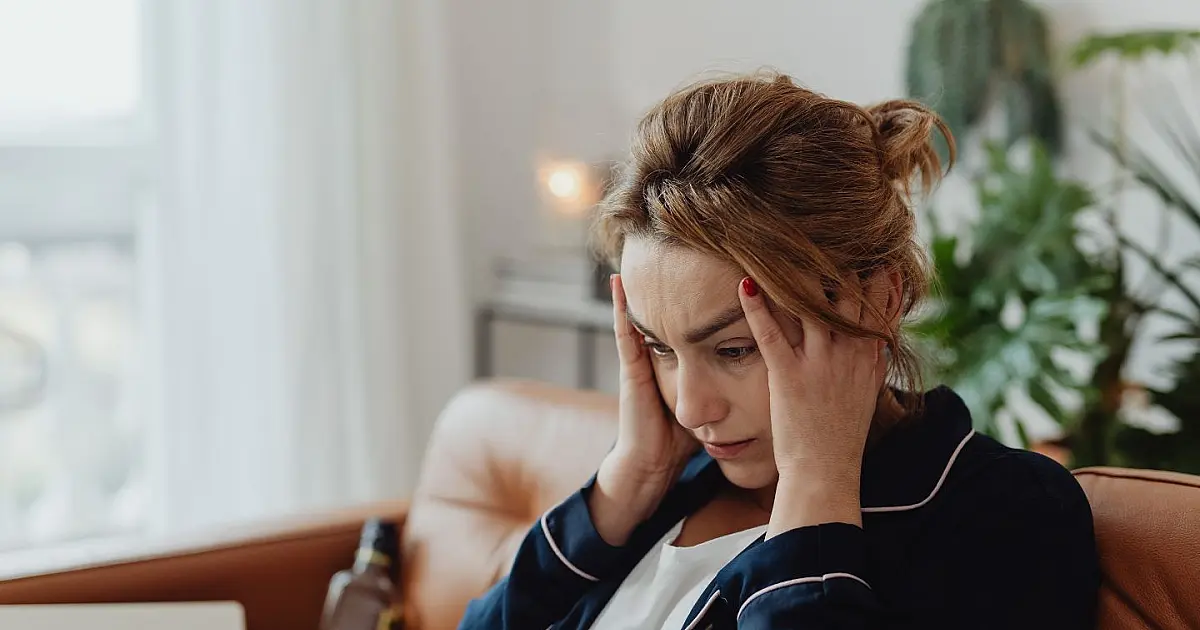 Mulher com dor de cabeça, sentada, representando alerta para riscos neurológicos e AVC.