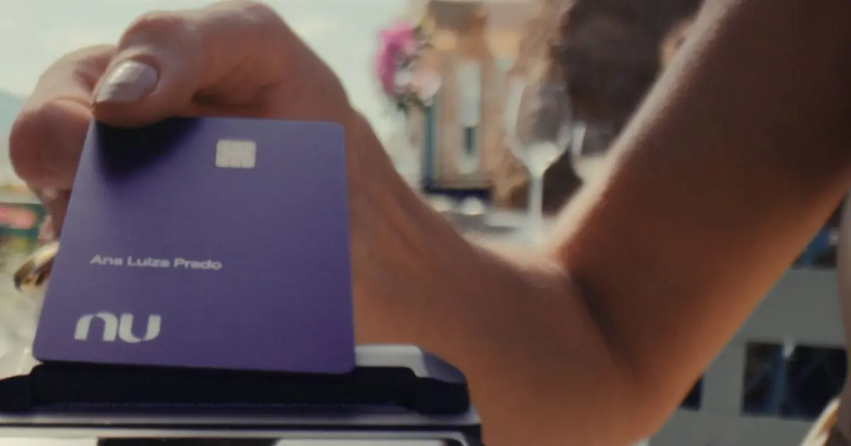 Pessoa segura cartão do Nubank em ambiente interno, representando o uso de serviços do banco digital.