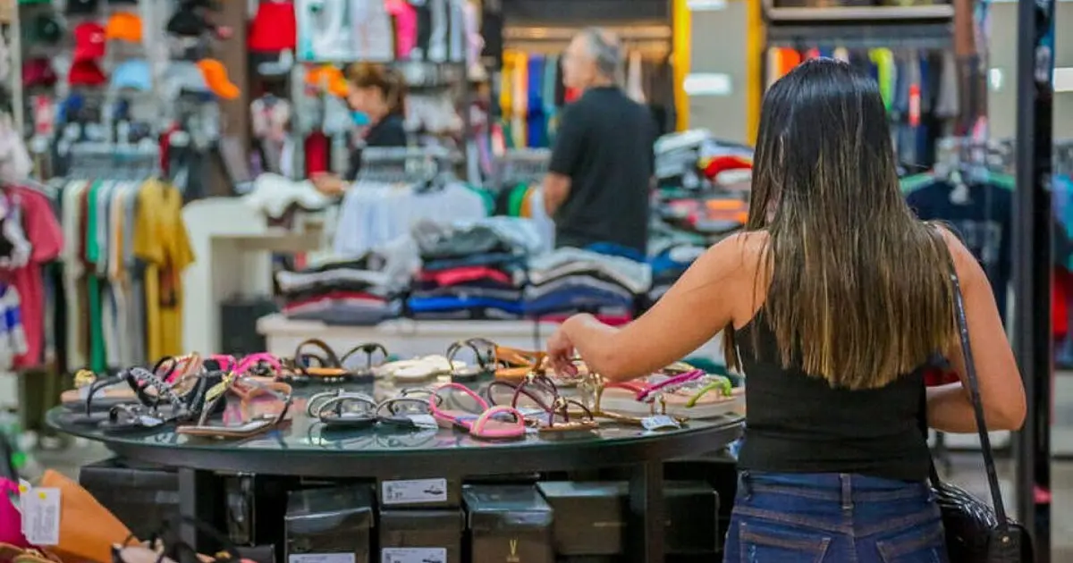 Cliente observa calçados e roupas expostos em loja do comércio varejista.