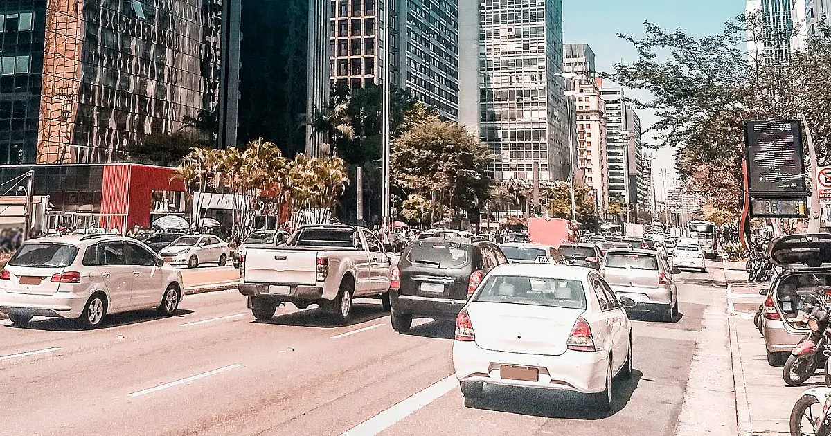 Carros circulando em avenida movimentada em área urbana.