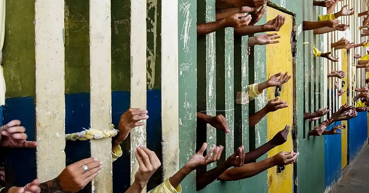 Pessoa privada de liberdade faz sinal indicando superlotação em cela de presídio.