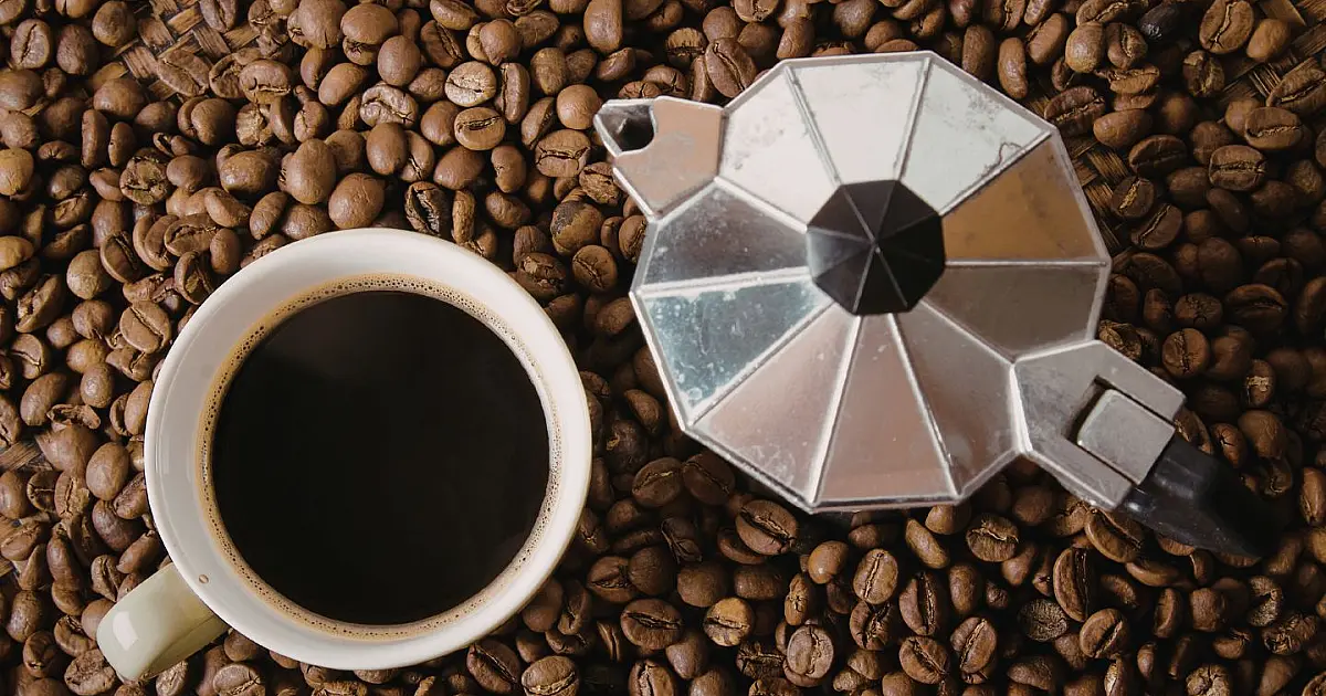 Grãos de café espalhados sobre mesa de madeira representando consumo de cafeína.