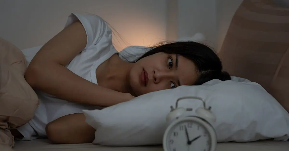 Pessoa deitada na cama sem conseguir dormir, associando alimentação noturna à insônia.