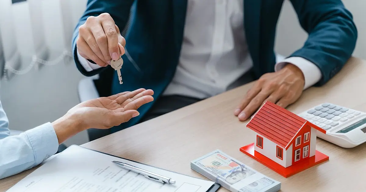 Contrato imobiliário sendo assinado com chaves de casa sobre a mesa.