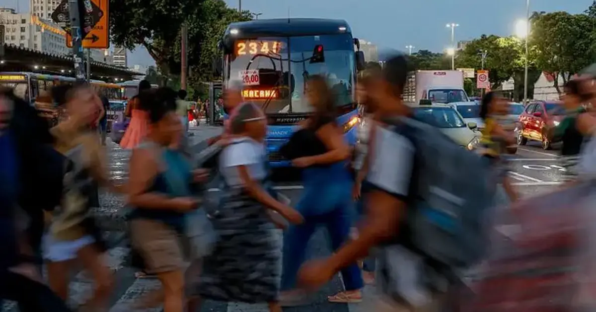 Pedestres atravessando rua em área comercial, representando trabalhadores e economia urbana.