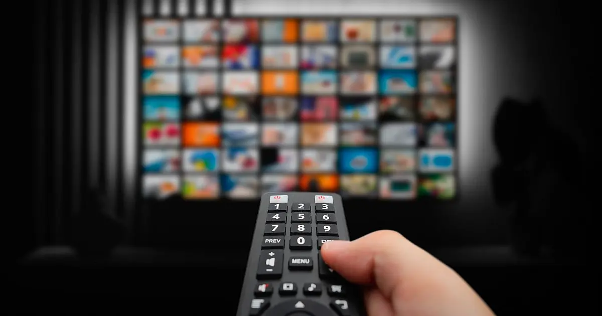 Pessoa assistindo TV com controle remoto em casa utilizando plataforma de streaming