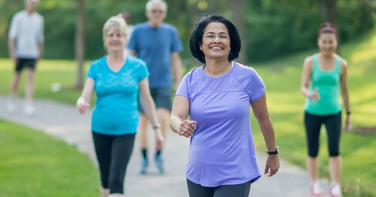 Pessoas caminhando em parque durante atividade física ao ar livre.