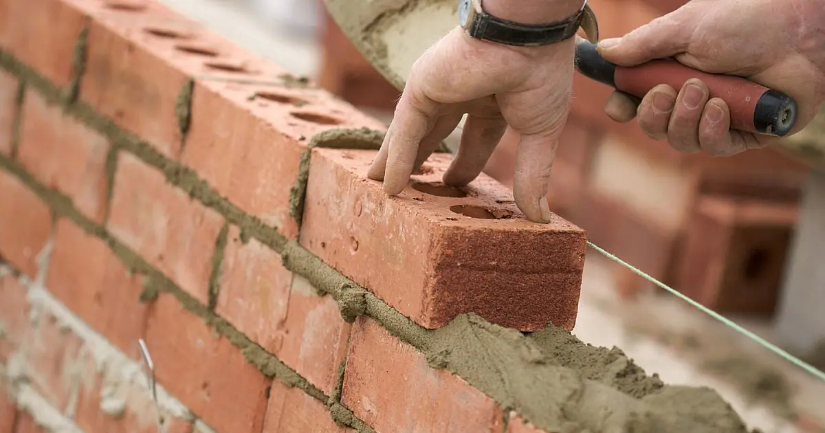 Pedreiro trabalhando na construção de muro de alvenaria em residência