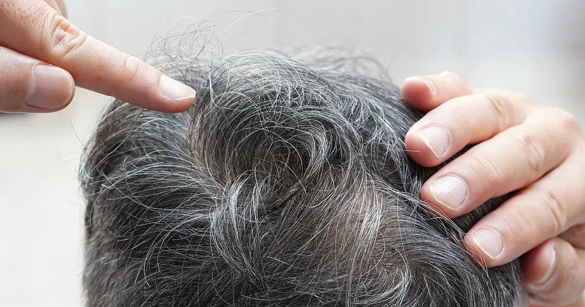 Mulher segurando o cabelo enquanto observa fios brancos