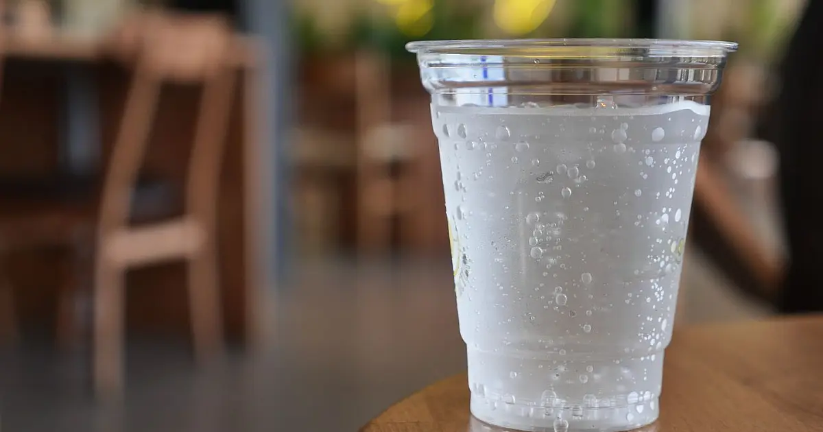 Copo de água com gás sobre mesa com bolhas visíveis.