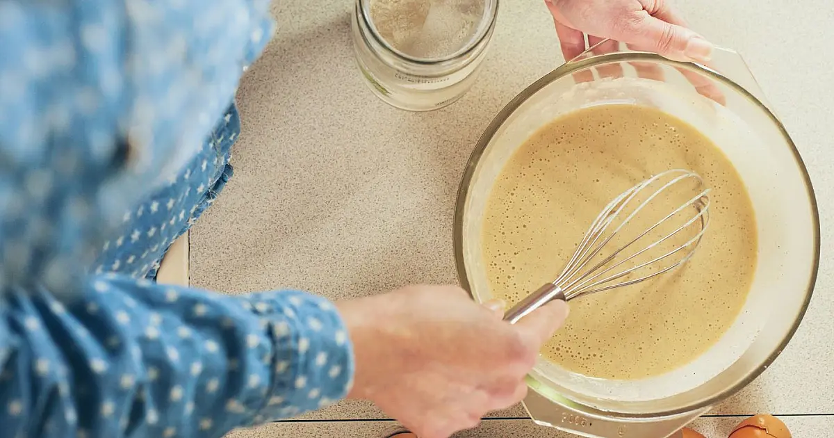 Pessoa batendo ovos e massa de bolo em tigela na cozinha