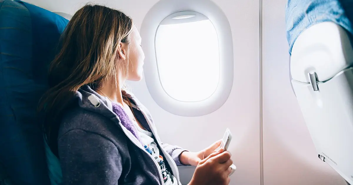Mulher utilizando celular dentro de avião durante voo com aparelho em modo avião.