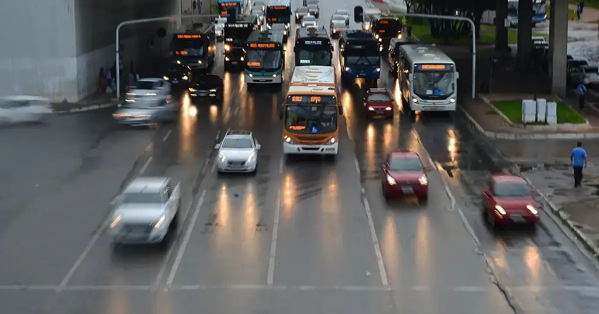Veículos circulando em rodovia com faróis acesos durante o dia.