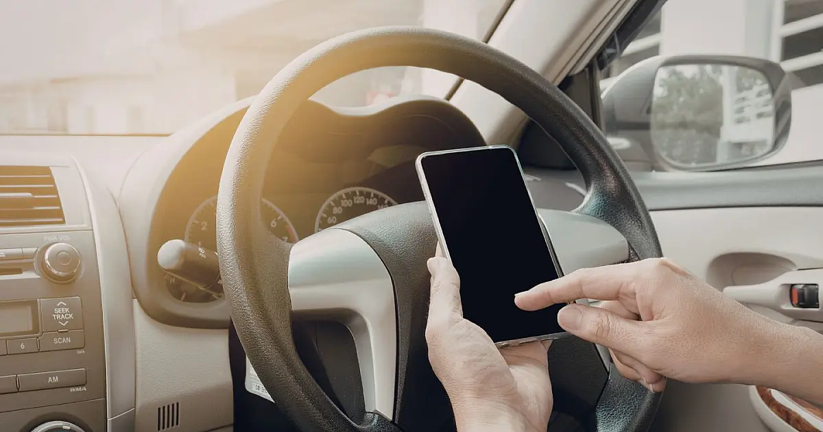 Motorista dirigindo enquanto utiliza celular dentro do carro.