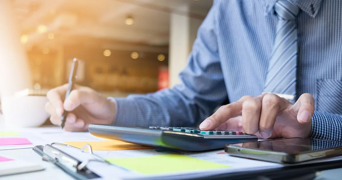 Pessoa analisando contas e calculando dívidas em mesa com papéis.