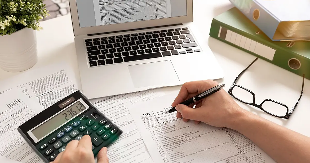 Pessoa fazendo cálculos e organizando documentos para declarar o Imposto de Renda.