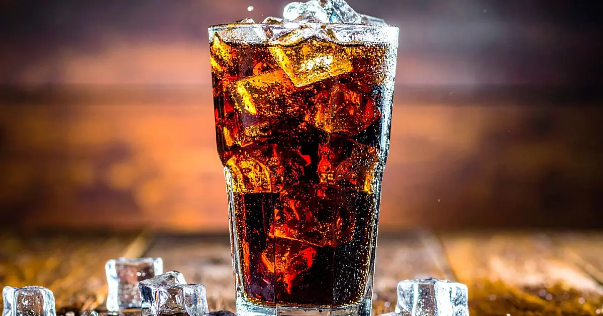 Copo com refrigerante escuro e gelo sobre mesa.