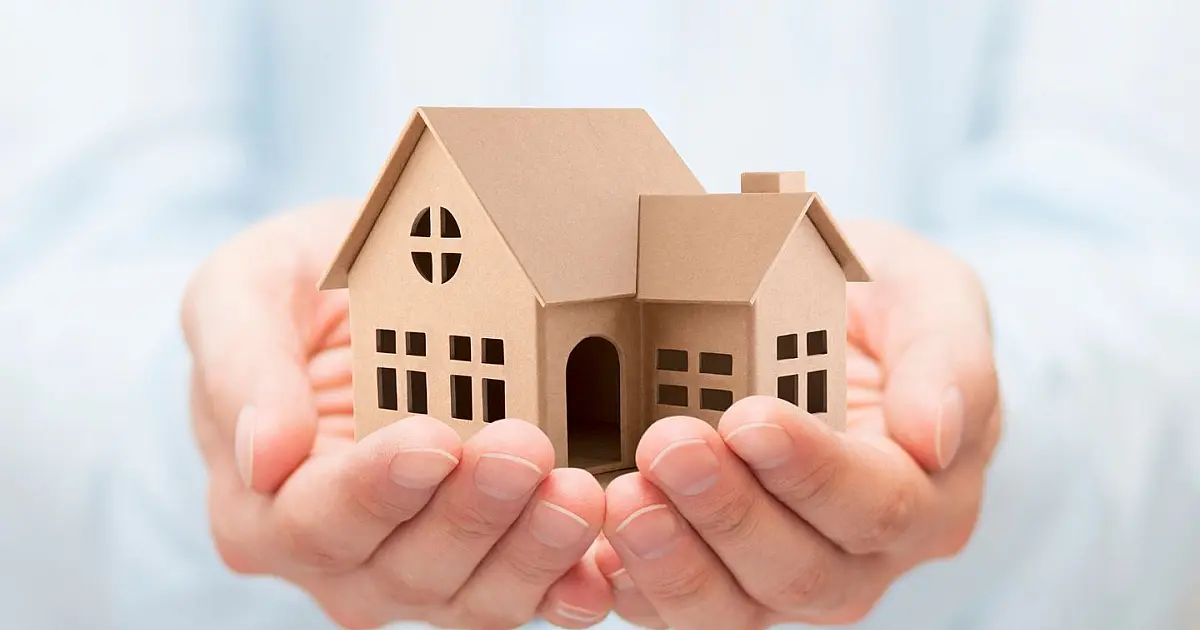 Mãos segurando uma miniatura de casa representando acesso à moradia e financiamento habitacional.