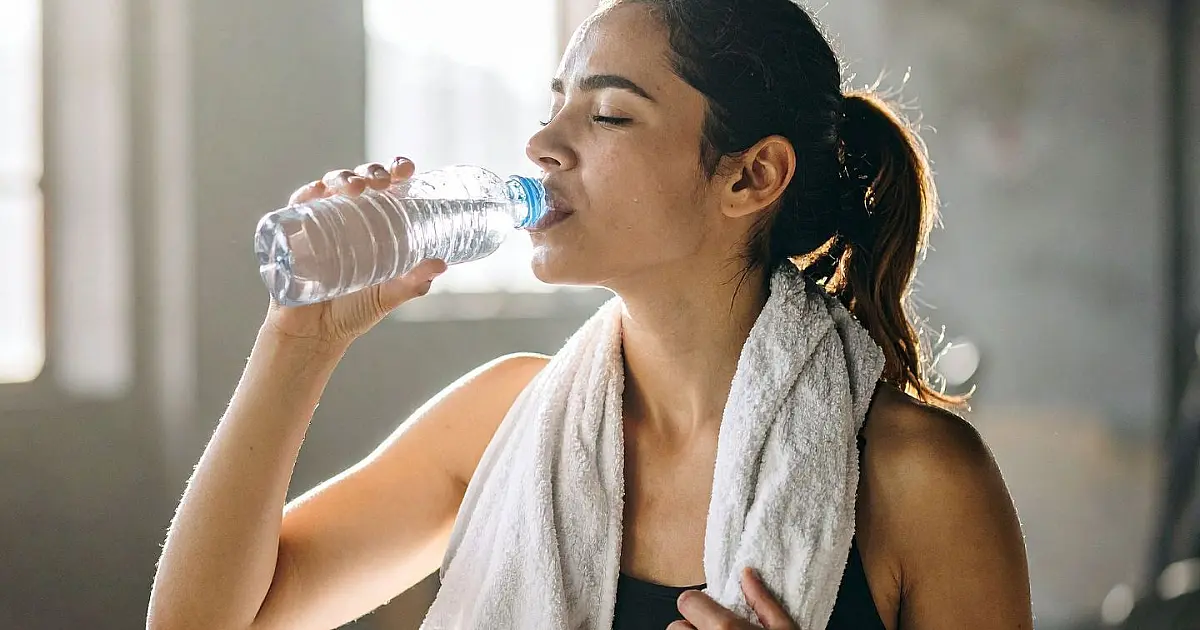 Mulher bebendo água em copo transparente.