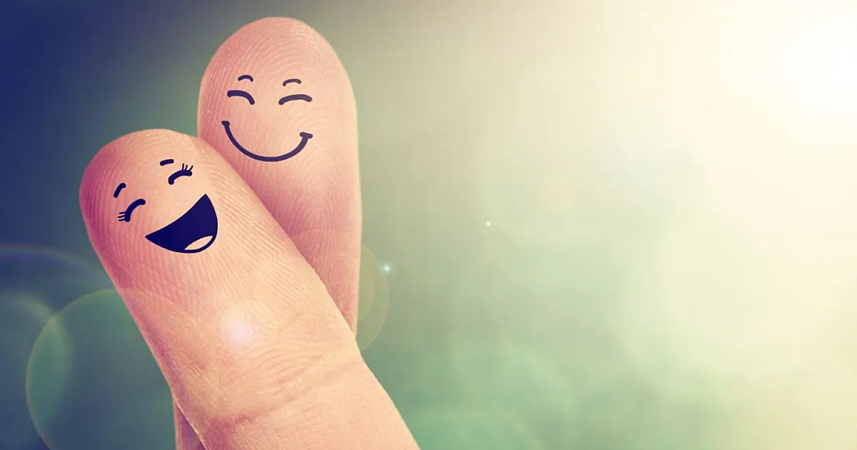 Dedos com desenhos de rostos felizes representando felicidade.