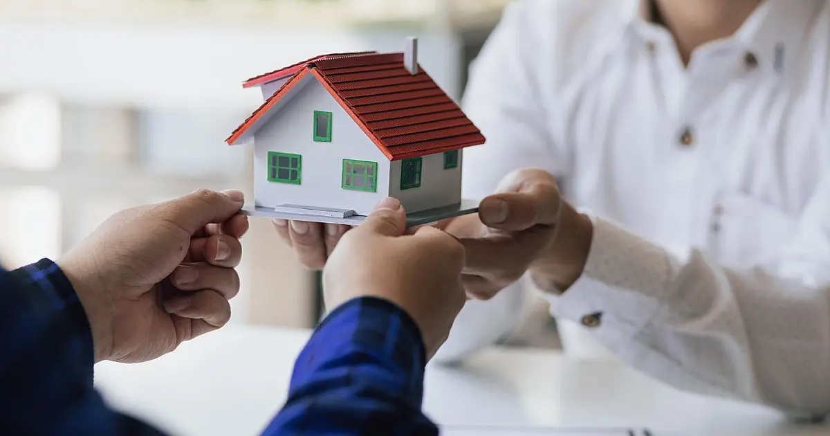 Pessoa entregando maquete de casa simbolizando doação de imóvel