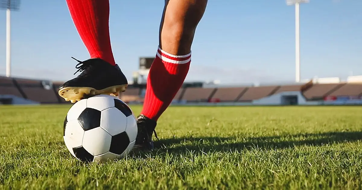 Jogador de futebol conduzindo a bola durante partida em campo gramado.