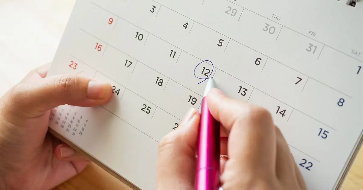 Mão segurando caneta sobre calendário do mês de abril com marcação de datas de feriados.