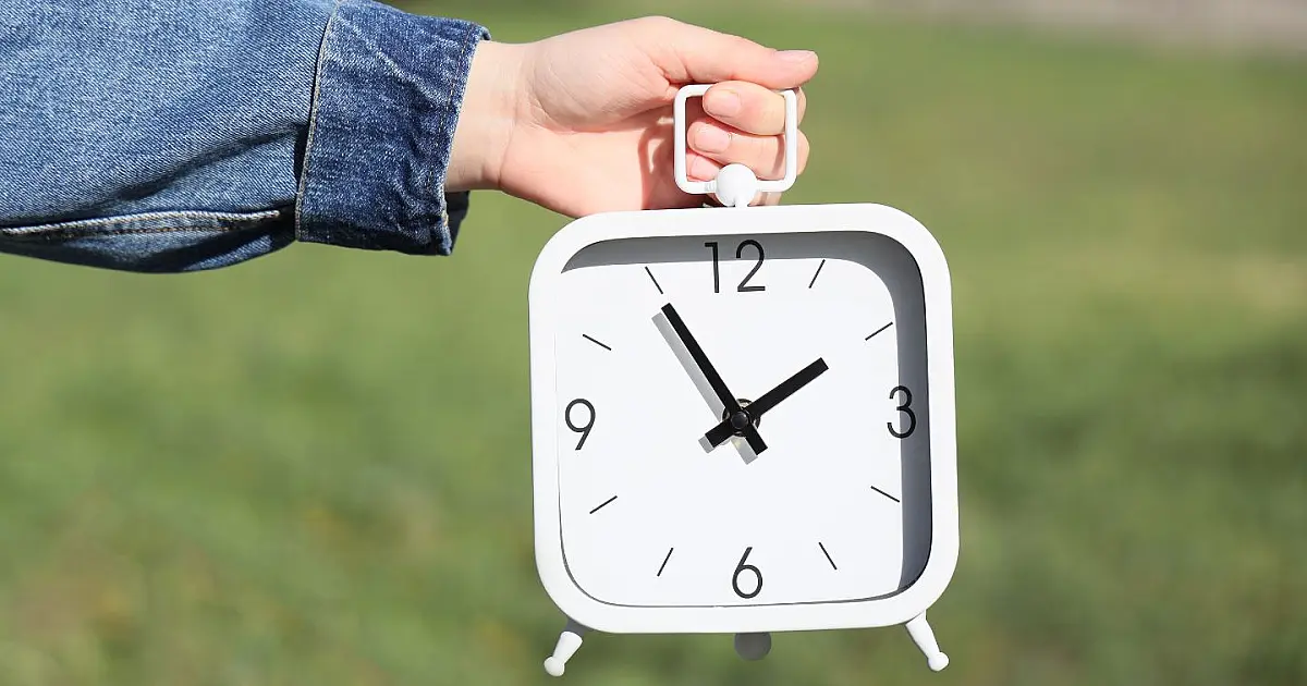Relógio sendo segurado ao ar livre representando mudança para horário de verão