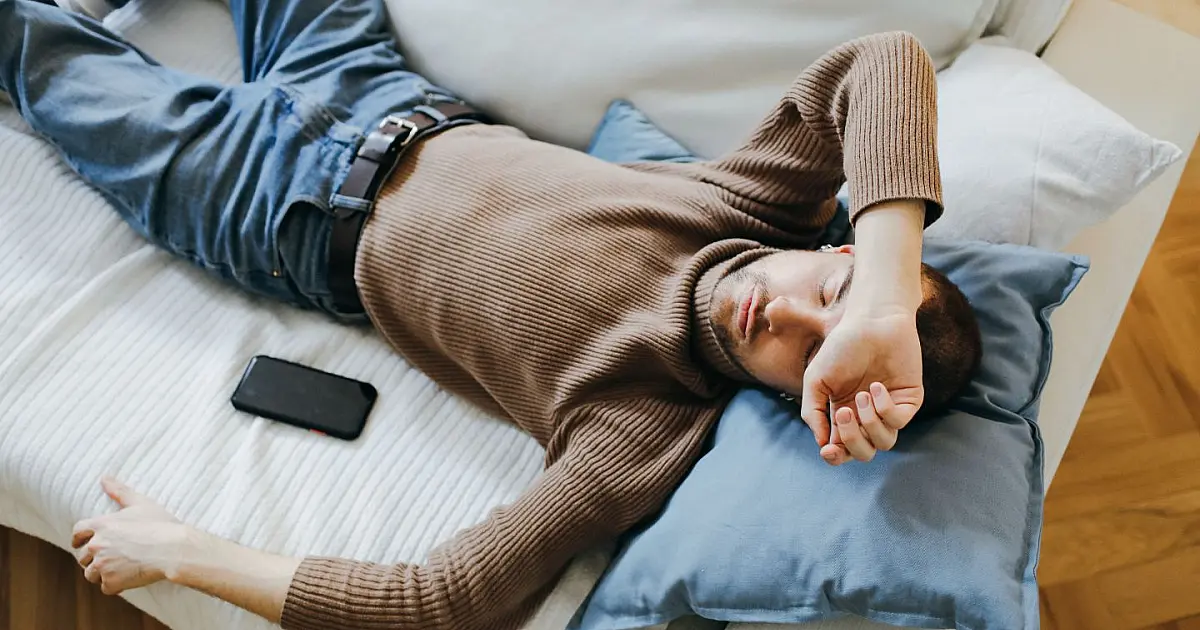 Homem dormindo em sofá representando descanso e recomendação de horas de sono.