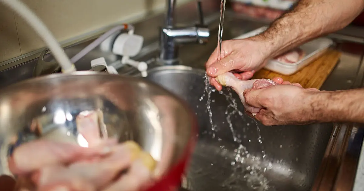 Pessoa lavando pedaços de frango cru na pia da cozinha.