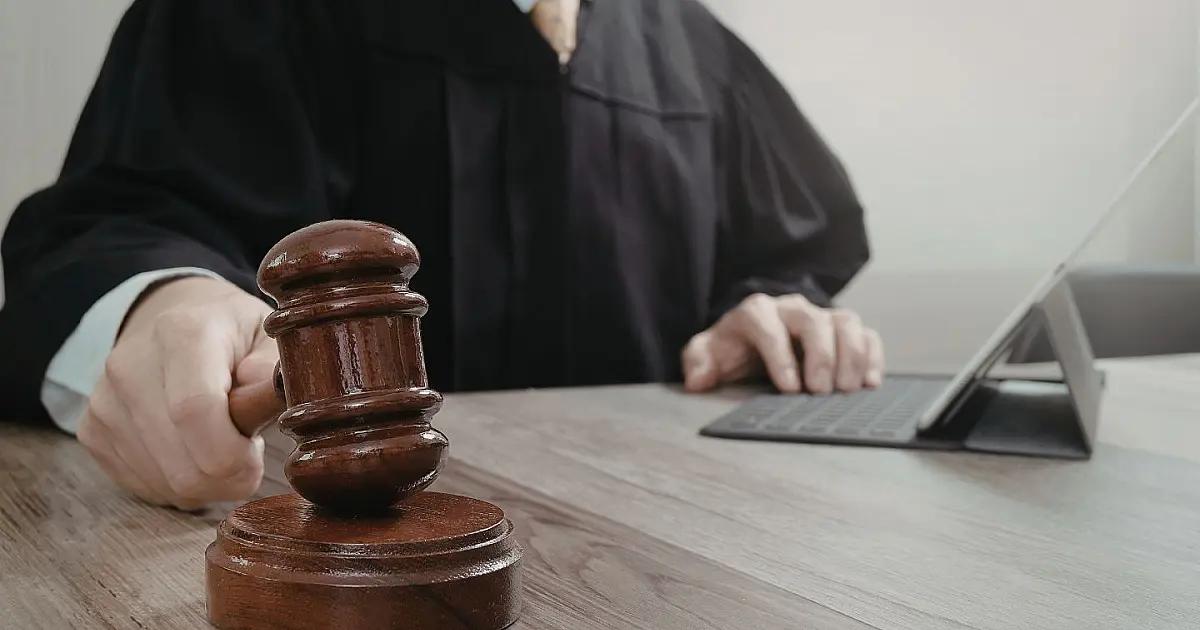 Juiz segurando martelo de tribunal durante julgamento em mesa de trabalho