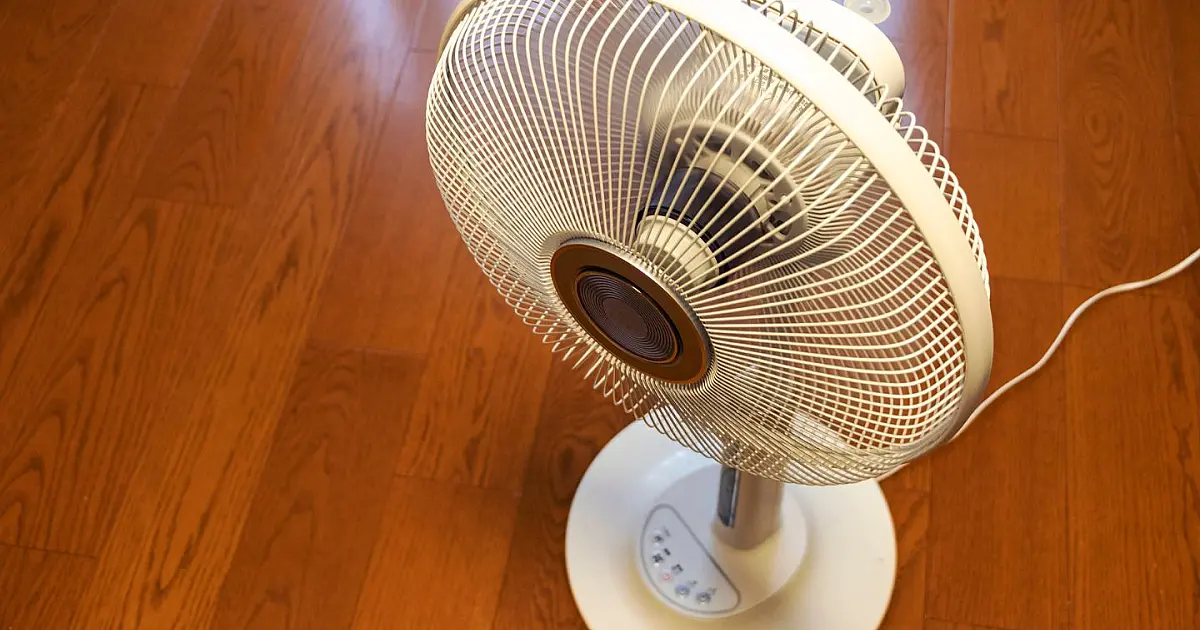 Ventilador branco posicionado no chão de um quarto para circulação de ar
