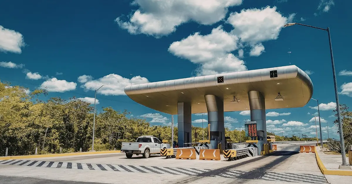 Praça de pedágio em rodovia ensolarada com caminhão branco passando pela pista.