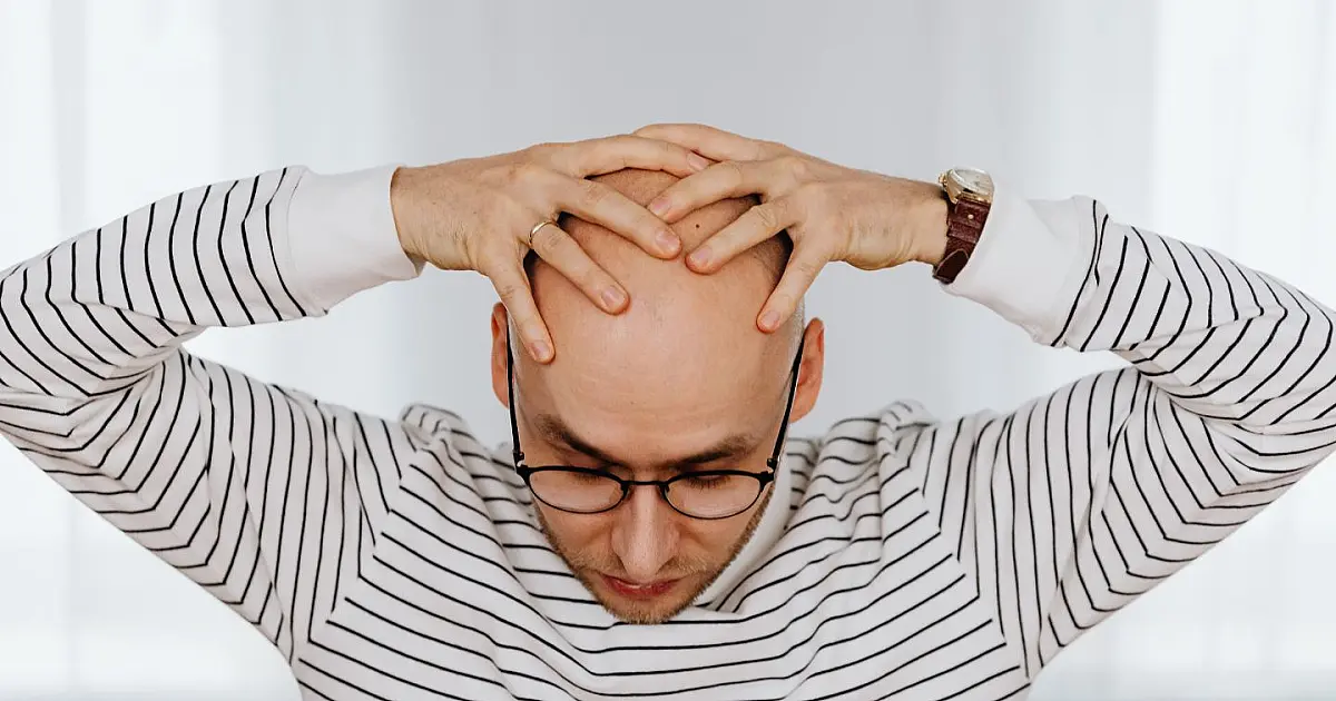 Homem com as mãos na cabeça representando preocupação com queda de cabelo e calvície.