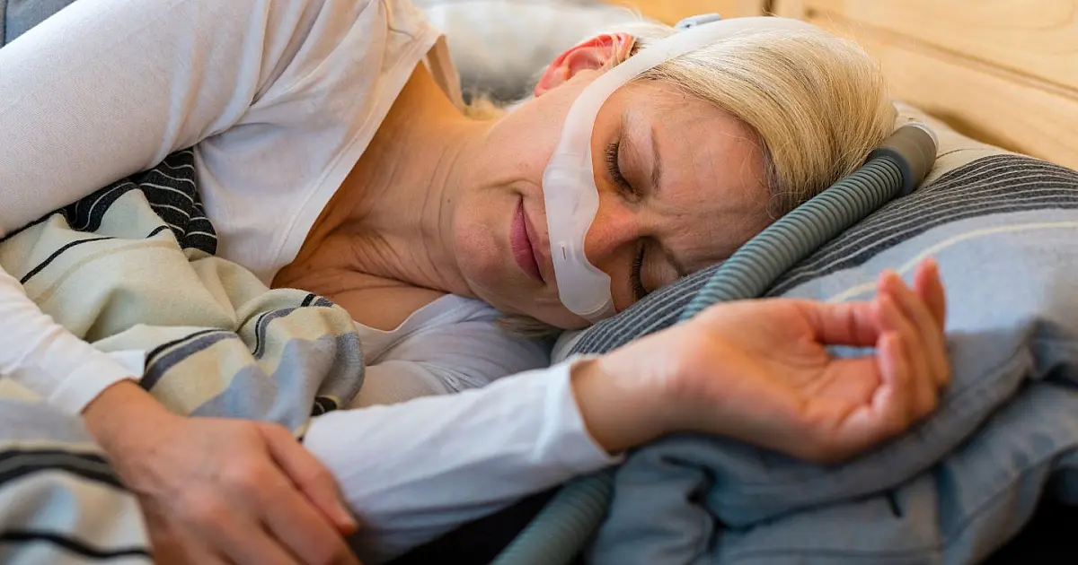 Mulher dormindo com máscara CPAP usada no tratamento da apneia do sono.