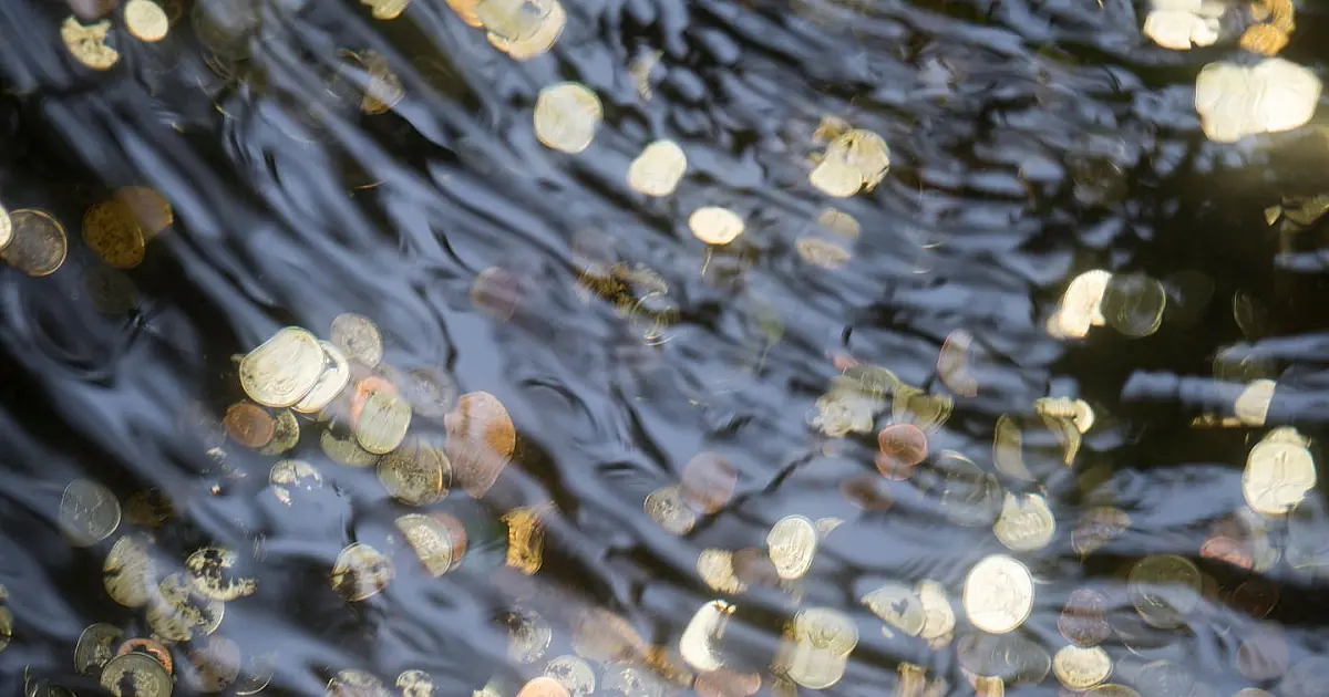 Moedas acumuladas dentro de fonte decorativa representando tradição de fazer pedidos.