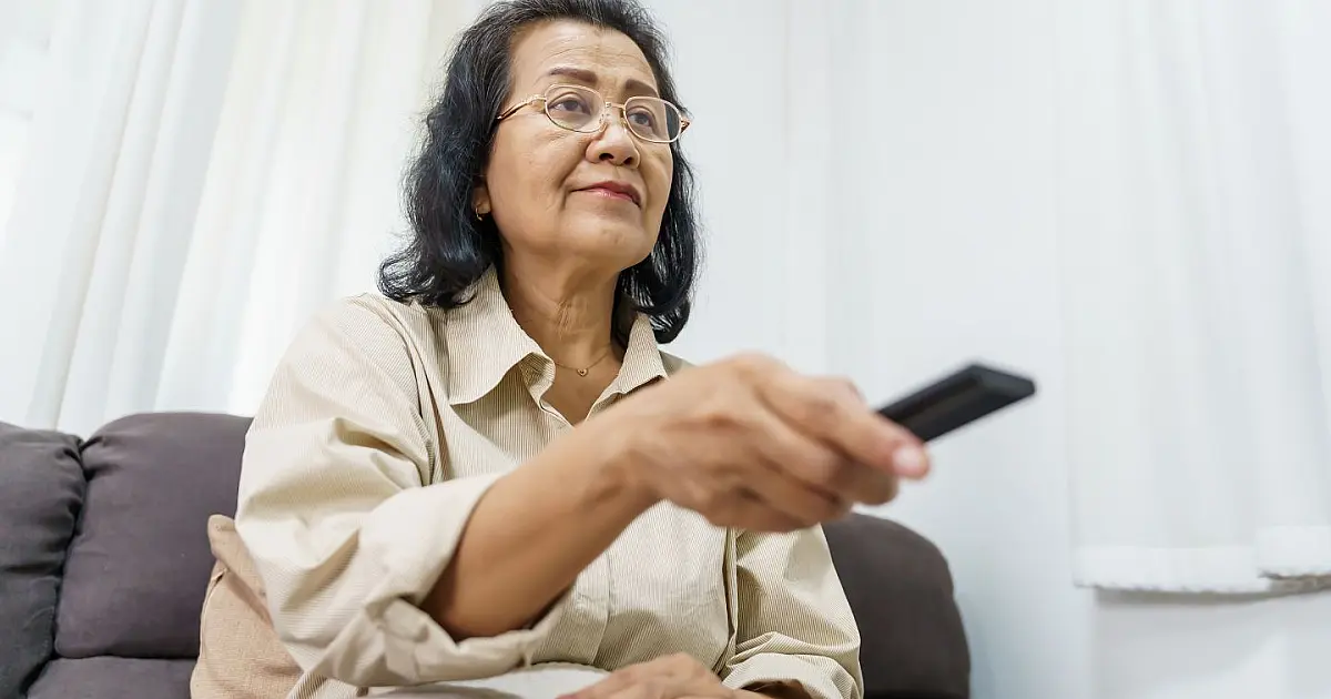 Idosa assistindo televisão com controle remoto em ambiente doméstico
