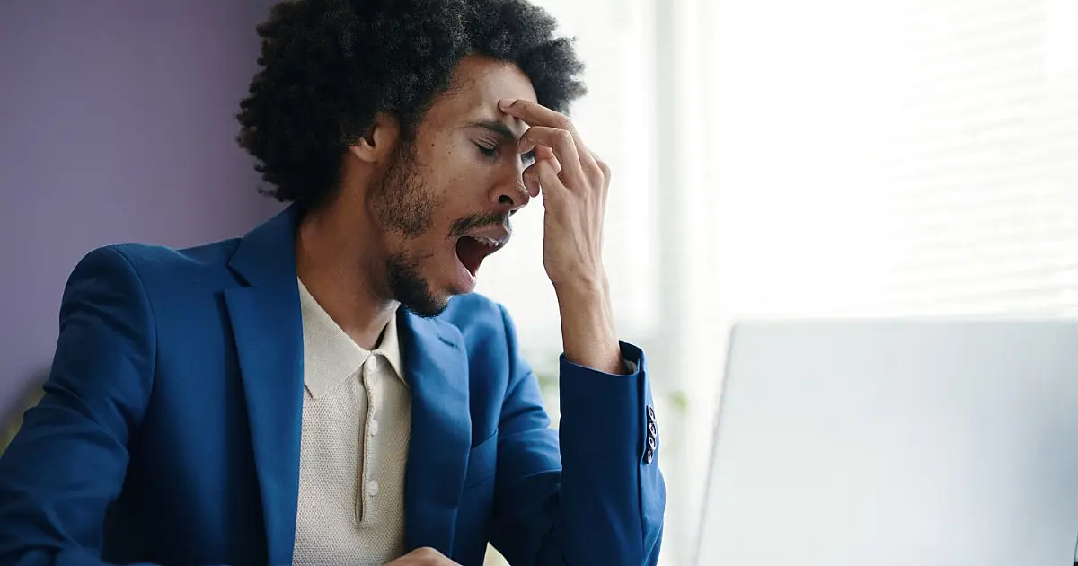 Homem bocejando em ambiente de trabalho representando o bocejo contagioso.