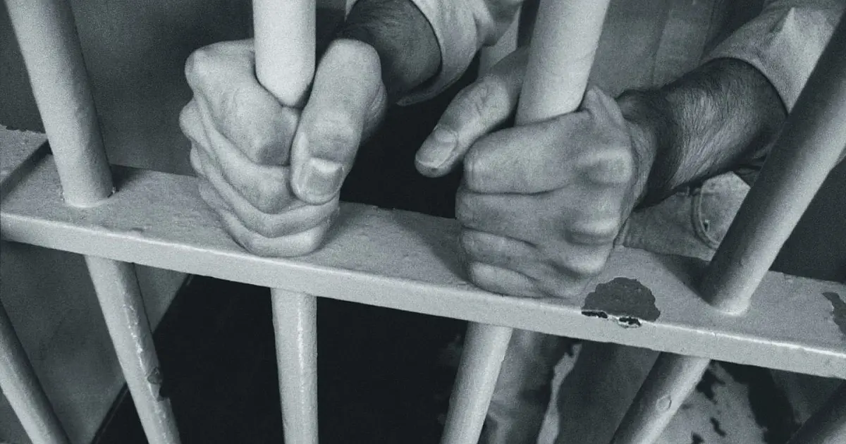 Mãos segurando grades de prisão representando debate sobre legislação penal juvenil.