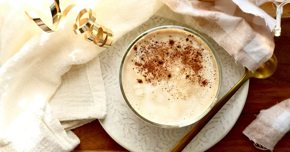 Xícara de café servida sobre mesa de madeira com colher ao lado