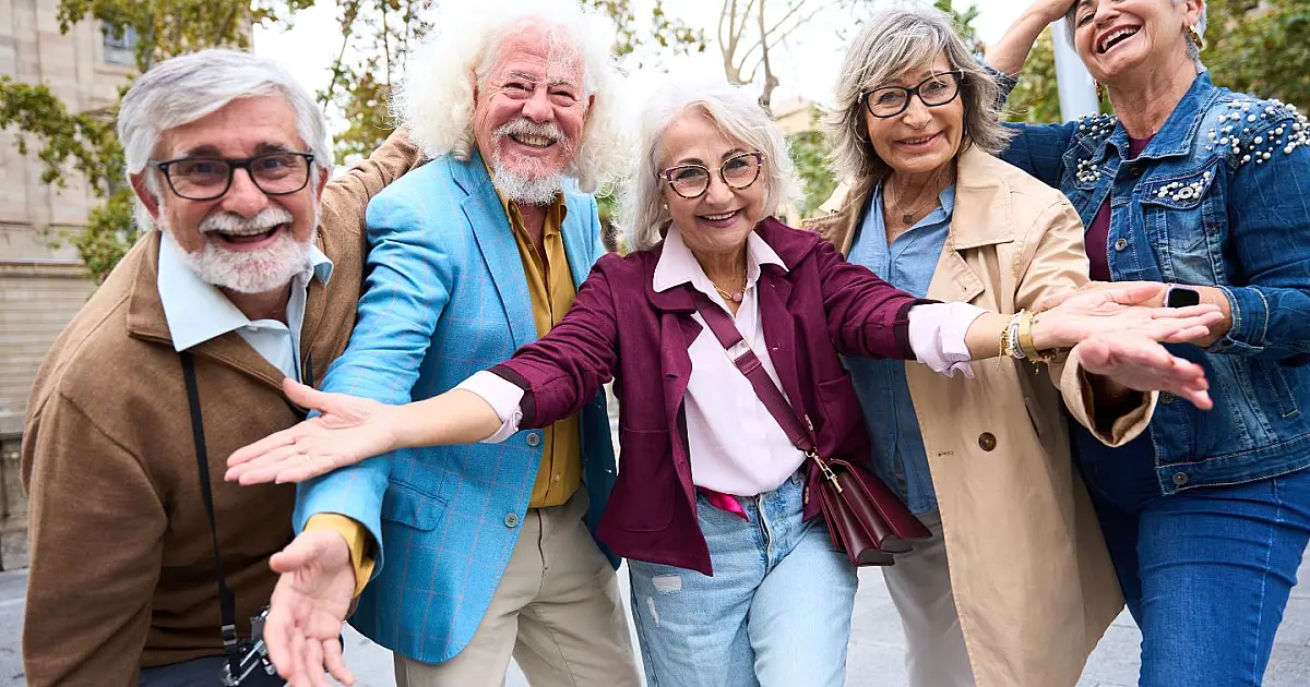 Grupo de idosos sorrindo ao ar livre durante encontro social relacionado à qualidade de vida.