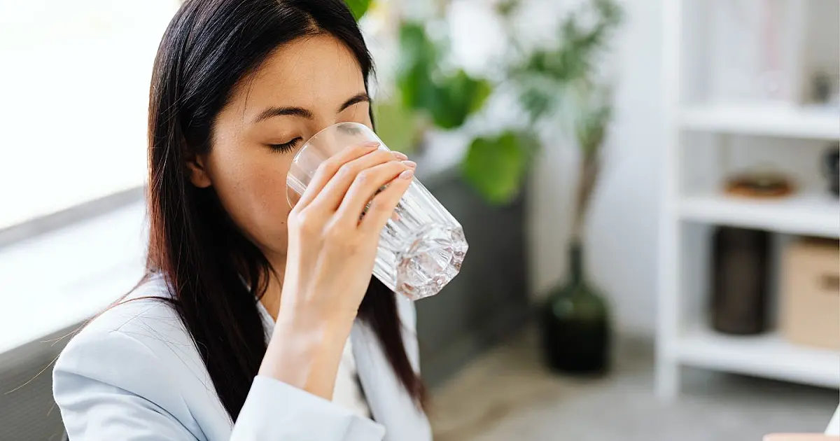 Mulher bebendo um copo de água pela manhã representando hidratação em jejum.