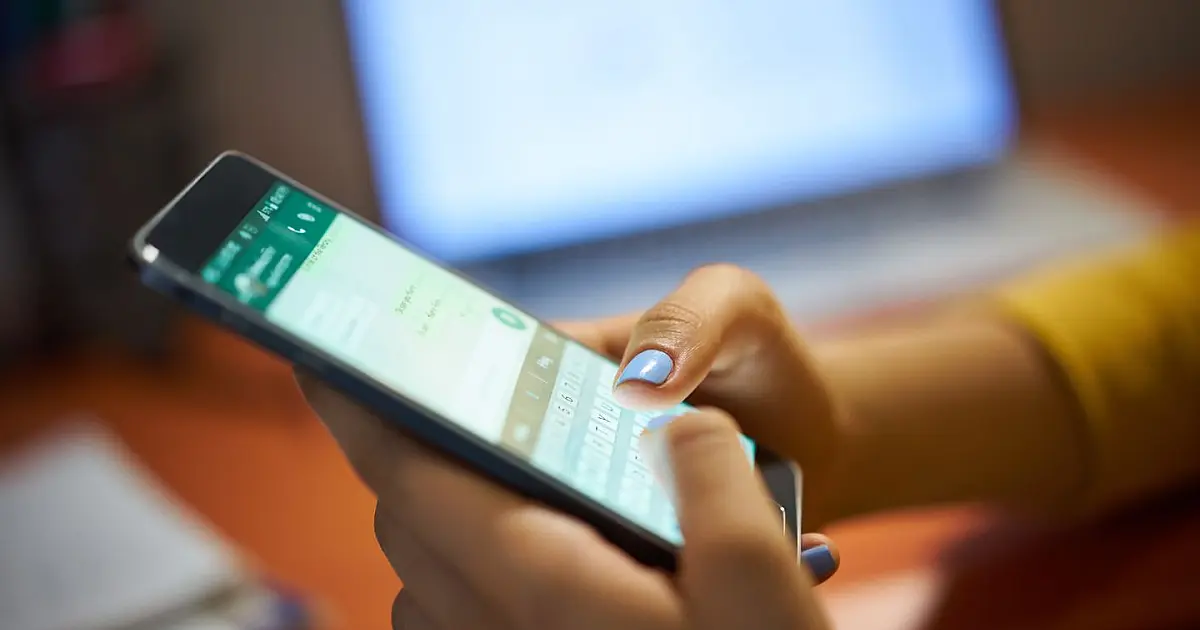 Mulher digitando mensagem no WhatsApp em celular à noite