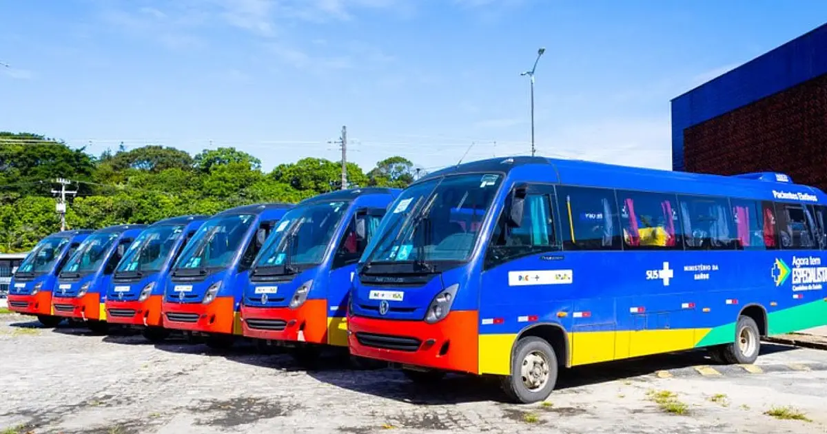 Fileira de micro-ônibus e vans brancos com a identidade visual do SUS e do Governo Federal estacionados em pátio aberto durante evento oficial na UFPB.