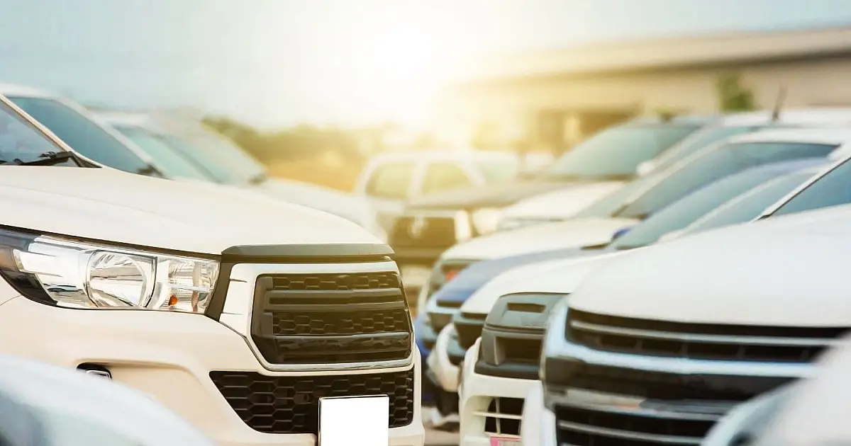Fileiras de automóveis novos estacionados em um pátio industrial sob a luz do dia.