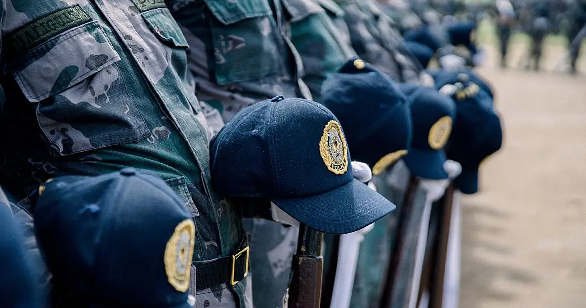 Close-up com foco detalhado em quepes oficiais de policiais alinhados sobre uma mesa, simbolizando a cooperação e a presença das forças de segurança estatais.