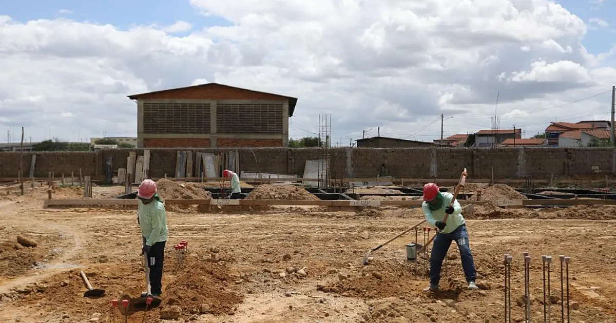Vista em plano médio de trabalhadores da construção civil vestindo uniformes de segurança e capacetes, atuando em um canteiro de obras de infraestrutura urbana.