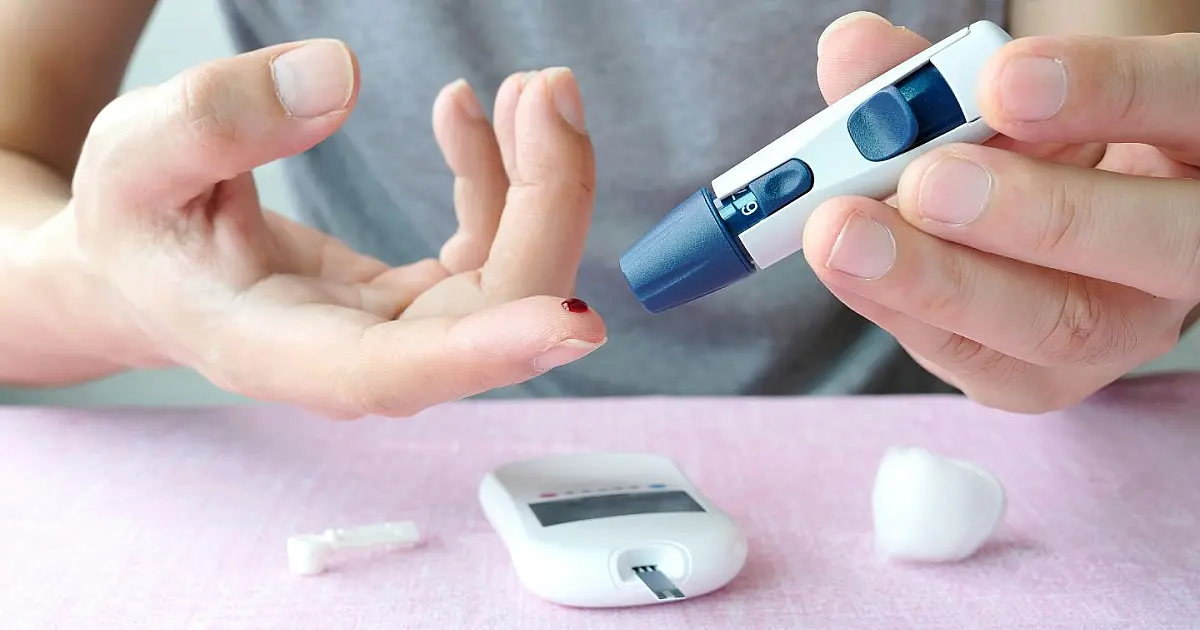 Close nas mãos de uma pessoa utilizando um pequeno aparelho digital portátil para monitorar os níveis de glicose no sangue.